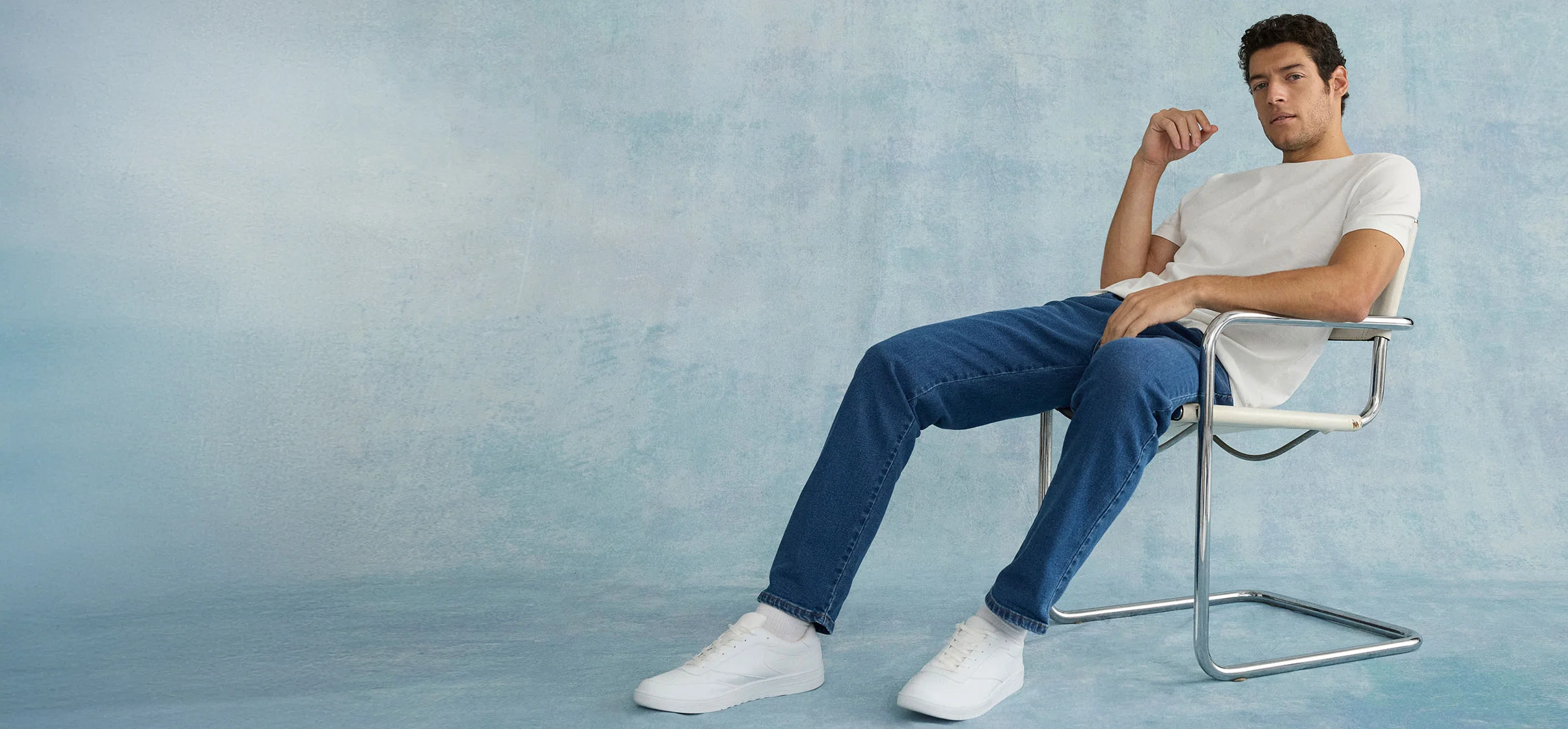 Look décontracté : T-shirt blanc, jean bleu et sneakers blanches sur une chaise moderne.