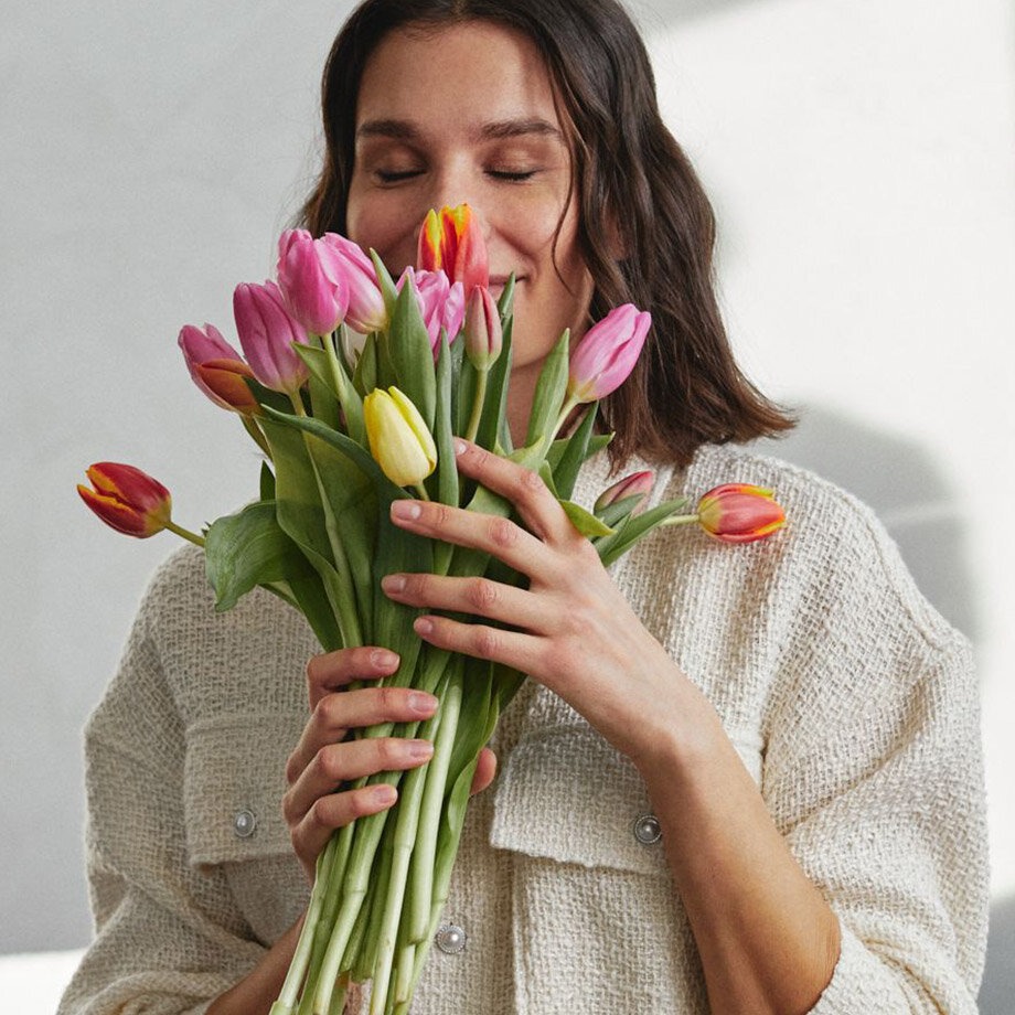 Une femme vêtue d’un pull blanc douillet et tenant à la main des tulipes colorées.