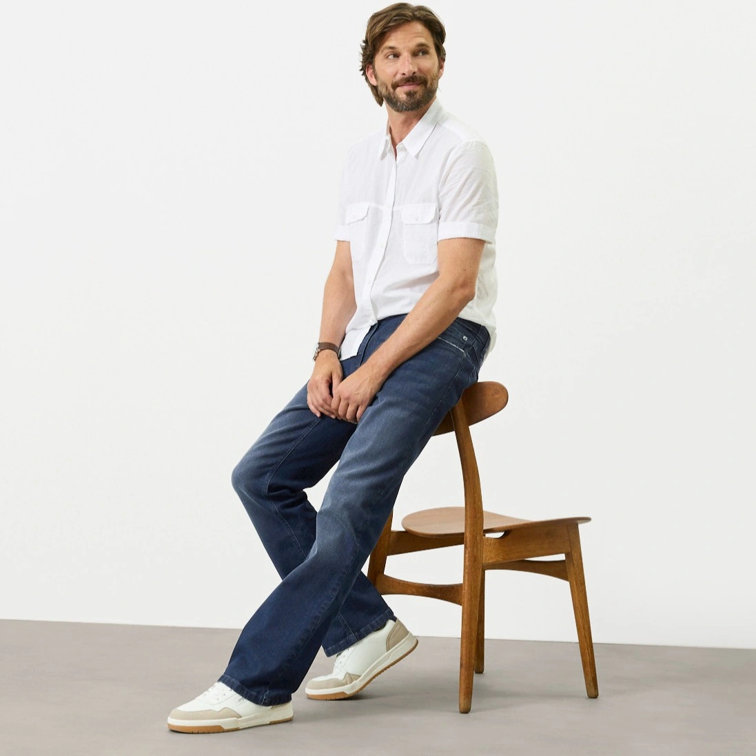 Chemise blanche à manches courtes, jean bleu coupe Regular Fit et baskets blanches modernes.
